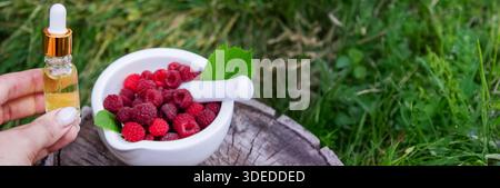 Raspberry essential oil in a bottle with fresh berries on a wooden stump Stock Photo