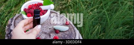 Raspberry essential oil in a bottle with fresh berries on a wooden stump Stock Photo