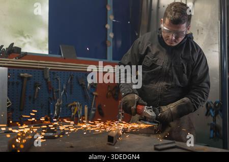 A skilled male welder uses a cutting tool in a factory environment creating sparks while working on metal. Stock Photo