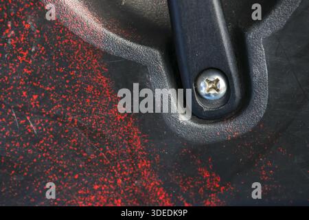 Close up detail of textured black surface with red splatter patterns and metallic screw securing hard plastic part showing sturdy industrial construct Stock Photo
