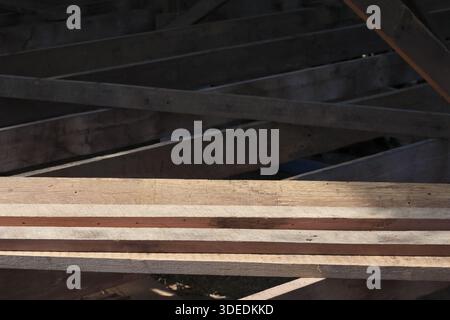 Unfinished wooden plank structure under dark roof showing construction texture with sturdy lines and rough surface feeling abandoned and forgotten in Stock Photo