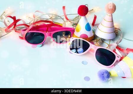 Carnival children party concept with pink sunglasses, funny paper hats, streamers, fairy lights and confetti on a light blue background, copy space, s Stock Photo