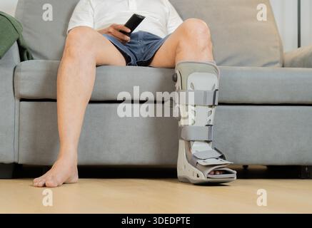 Cropped shot of man relaxing and holding TV remote after car accident suffering at home. A man with injuries is watching TV Stock Photo