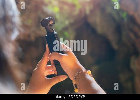 Back view of young woman holding an action camera for take photos and videos in the cave. Ideal device for travel videos and photos. Stock Photo