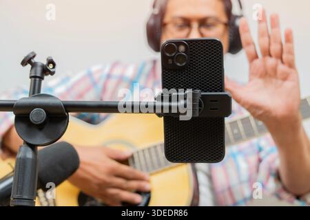 Asian man blogger recording and live steam playing guitar on social media. Concept of guitarist online lesson while stay at home Stock Photo