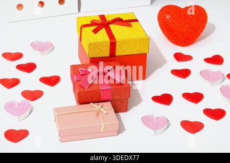 Three gift boxes in different colors are placed on a surface. Small heart decorations and candles surround the boxes. Stock Photo