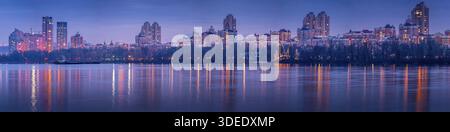 Night over Obolon embankment in Kyiv with modern residential skyline with lights reflected in calm river water, dramatic sky Stock Photo