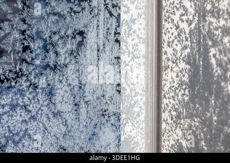 Frozen window covered in intricate frost patterns with a blurred winter landscape in the background. The delicate ice crystals create a natural artist Stock Photo