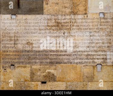 Ancient stone wall with Latin inscriptions, weathered surface. Stock Photo