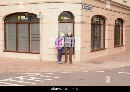 Elderly couple checking their smartphones on a street corner in St Helier, Jersey, The Channel Islands Stock Photo