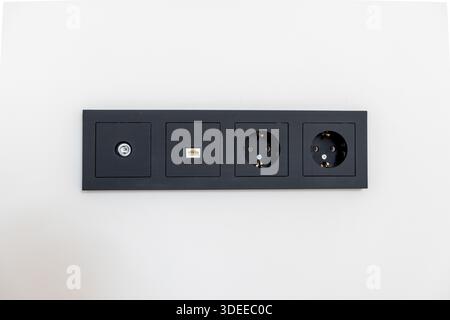A black electrical box with four outlets. The box is on a white wall Stock Photo