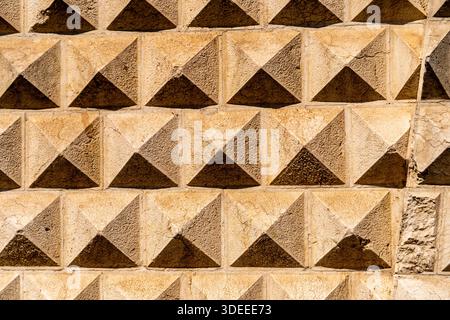 A close-up view of a textured stone wall featuring a pattern of pyramidal shapes, showcasing earthy tones and shadows Stock Photo