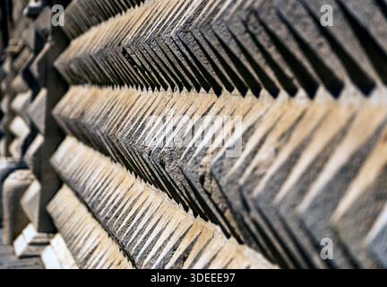 A close-up view of a textured stone wall with a zigzag pattern, showcasing shadows and light play on the surface Stock Photo