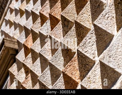 A textured wall featuring a pattern of three-dimensional triangular shapes, showcasing varying shades of beige and brown, with sunlight casting shadow Stock Photo