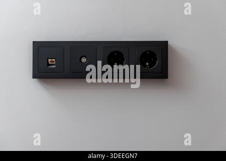 A black electrical box with four outlets. The box is on a white wall Stock Photo