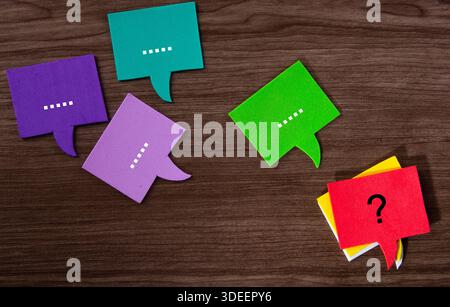 Speech bubbles showing conversation and a question mark bubble on a wooden background Stock Photo