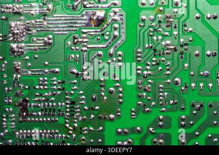 Green printed circuit board closeup showing metallic solder joints and conductive pathways used in electronic devices and digital systems. Stock Photo