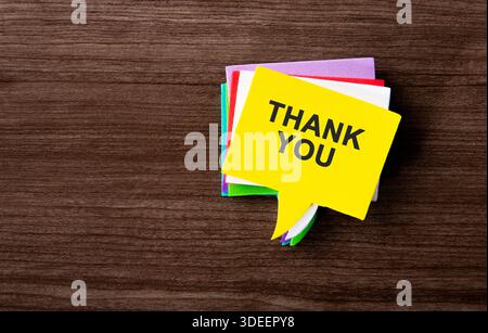 Yellow speech bubble sticker with thank you text on a stack of colorful notes Stock Photo