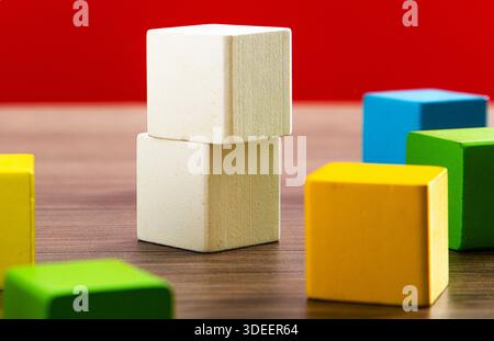 Wooden toy blocks creating a structure on a wooden table with a red background Stock Photo