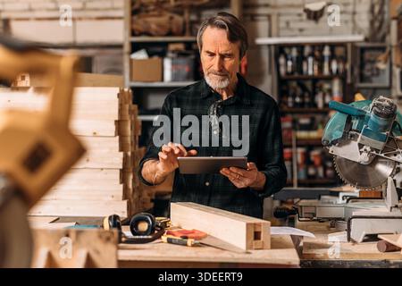 Senior carpenter using a digital tablet in his workshop || Model released Stock Photo