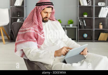 Business professional in keffiyeh using digital tablet while seated in office Stock Photo
