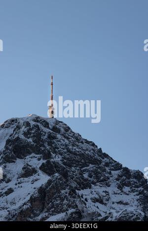 A telecommunication tower stands on a snow-covered mountain summit, symbolizing connectivity and infrastructure in a remote alpine environment. Stock Photo