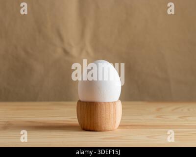 White fresh egg in the wooden egg stand, cup for breakfast on wooden eco beige background, with empty space, Easter holiday, healthy eating Stock Photo