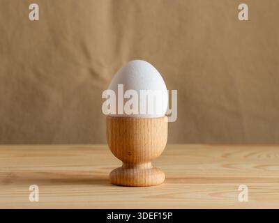 White fresh egg in the wooden egg stand, cup for breakfast on wooden eco beige background, with empty space, Easter holiday, healthy eating Stock Photo