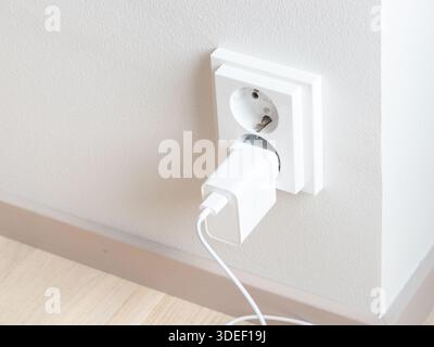 A close-up of a double electrical outlet mounted on a white wall, with a charger plugged into one of the sockets. Mindful of electricity consumption a Stock Photo
