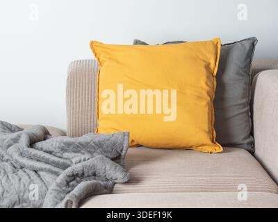 Cozy interior with a beige corduroy sofa, yellow and grey velvet pillows, and a grey quilted throw blanket. Neutral tones and textures create a warm, Stock Photo
