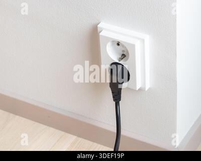 A close-up of a double electrical outlet mounted on a white wall, with a power cord plugged into one of the sockets. Mindful of electricity consumptio Stock Photo