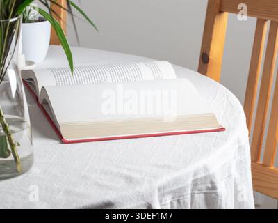 Open red hardcover book on a white tablecloth. Blank off-white pages with sewn binding lie flat, ideal for reading. Stock Photo