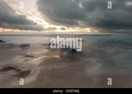 Long Exposure of waves crashing on coastal rocks in the Baltic Sea at sunset, Lithuania Stock Photo