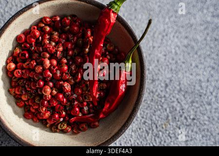 Overhead view of a bowl of fresh pink peppercorns and dried red chillies on a table Stock Photo