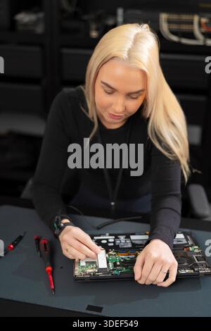 Woman IT technician works on laptop hardware during repair and upgrade in a workshop Stock Photo