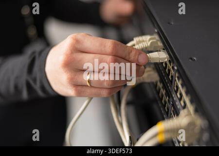Adult IT technician setting up network cables in a data center and performing maintenance Stock Photo