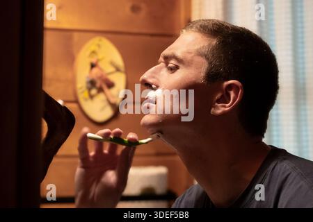 Side view of young man shaving near mirror in bathroom Stock Photo