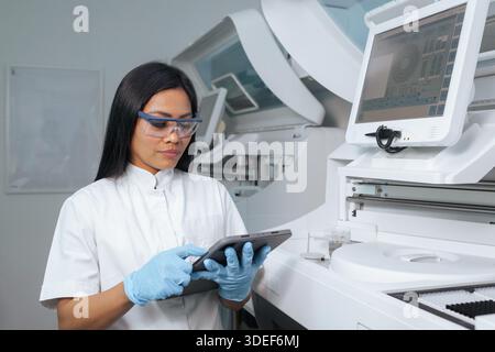 A female scientist in glasses uses a tablet to analyze data in a laboratory setting while working on healthcare innovation and diagnostics. Stock Photo