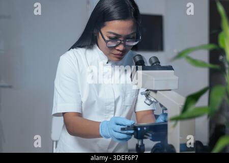 A female scientist examines samples using a microscope in a biotechnology laboratory focused on pharmaceutical medical research and biotechnology. Stock Photo