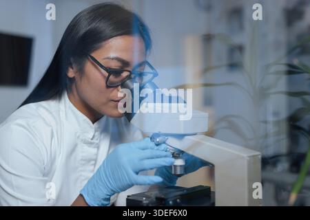 A scientist examines samples under a microscope to conduct research in a biotechnology laboratory focused on medical science and biotechnology. Stock Photo