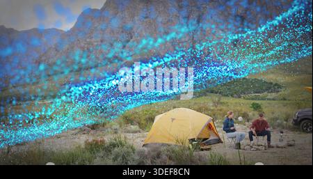 Sitting couple in red plaid and blue jacket cooking at campsite, yellow tent and blue streak Stock Photo