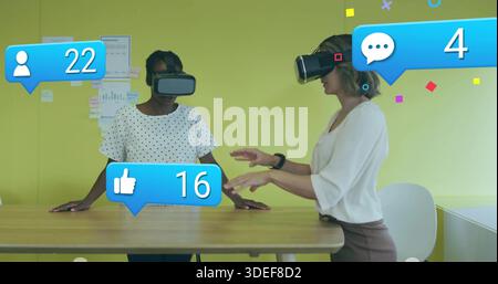 Interacting two midadult women polka and light tops using VR controls at office, with social icons Stock Photo