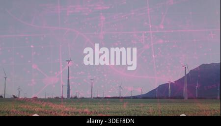 Displaying row of wind turbines spinning across grassy field near mountain ridge, with pink overlay Stock Photo