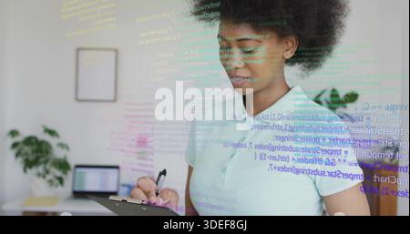 Reviewing clipboard and code overlay, woman working in home office in light polo, copy space Stock Photo