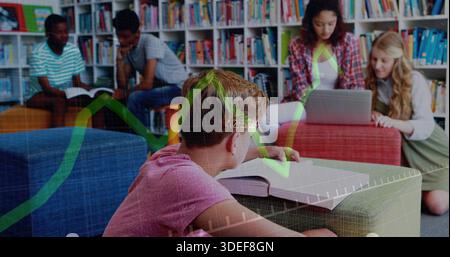 Leaning boy in pink tee reading textbook on ottoman in school library, with laptop, shelves, graph Stock Photo