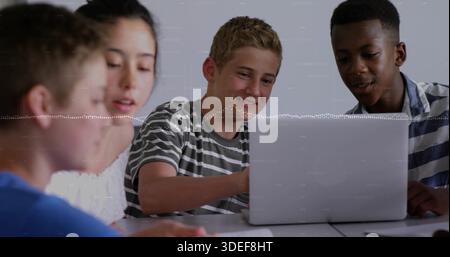 Studying students leaning over silver laptop on white table in classroom, with papers and notebook Stock Photo