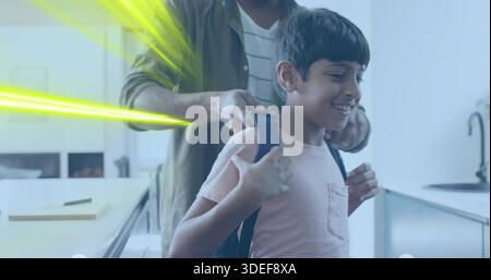 Adjusting dad in green shirt fastening dark backpack on school-age boy wearing pink tee in kitchen Stock Photo