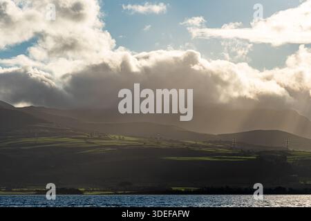 Light breaking through cloud over the Carneddau hills seen across the Menai Strait Stock Photo