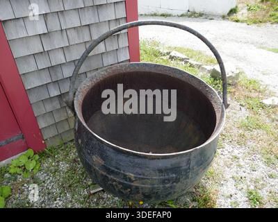 Rusty old metal cauldron by corner of building Stock Photo