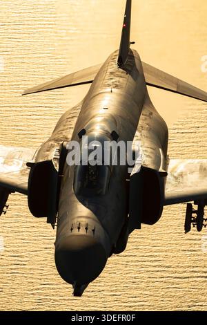 This air-to-air image depicts a Hellenic Air Force McDonnell Douglas F-4E Phantom II in silhouette during Athens Flying Week 2025. The twin-engine fighter is powered by two General Electric J79-GE-17A turbojets. The aircraft shows tandem cockpit, swept wings, twin vertical stabilizers, and afterburners. The photograph emphasizes the jet’s aerodynamic form, maneuvering performance, and precision display capabilities. Stock Photo